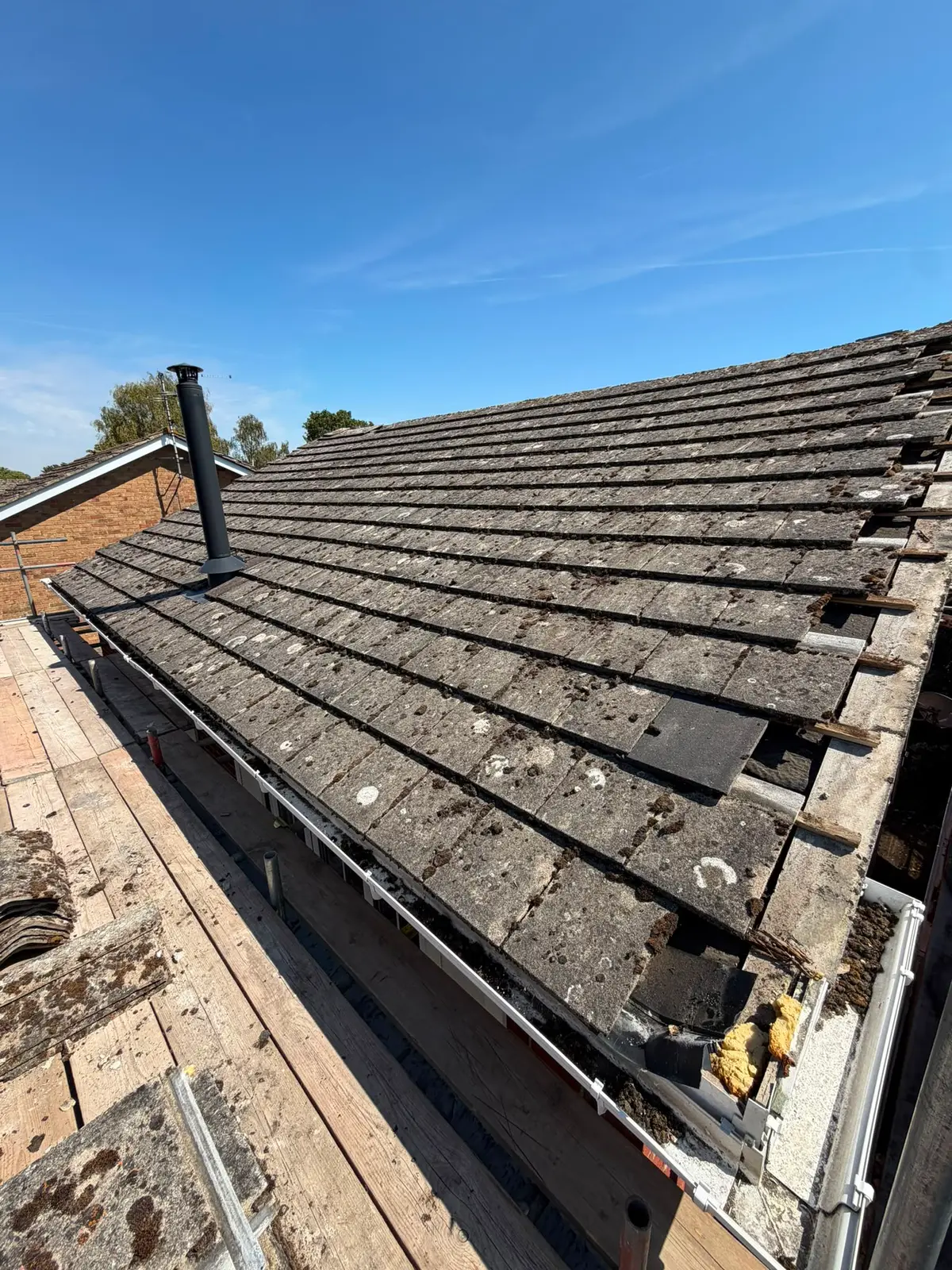 Worn concrete tiles being stripped from a roof ahead of a re-roof in Newbury