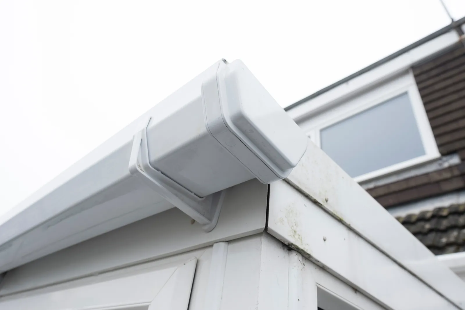 Close-up of a white square gutter stop end and outlet fitted to a fascia