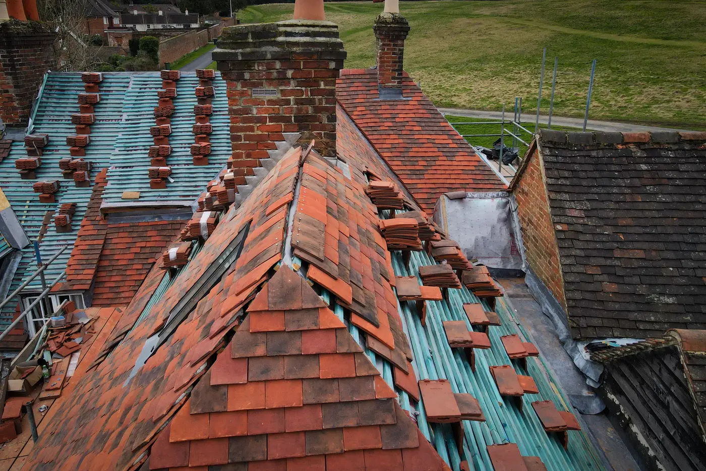 Aerial view of reclaimed clay roof tiles being re-laid around brick chimney stacks in Devizes