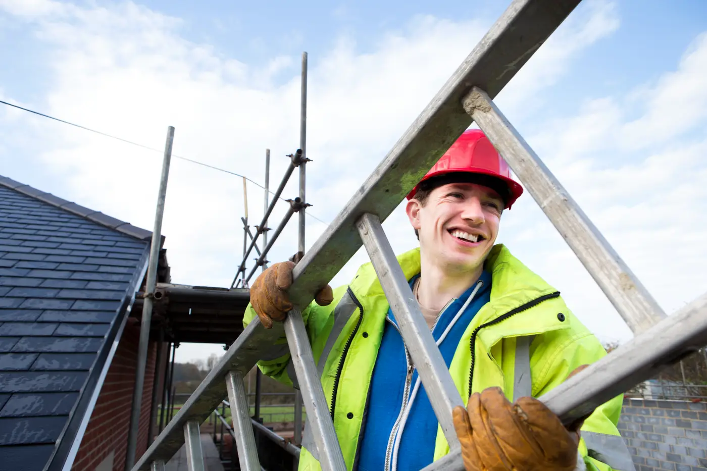 Smiling roofer holding scaffold poles beside a slate roof under construction in Devizes