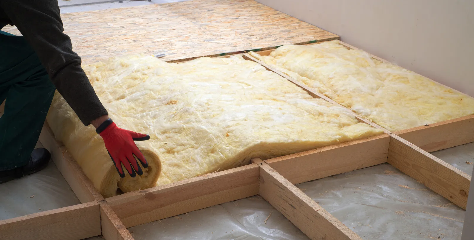 Installer rolling out mineral wool insulation over loft joists