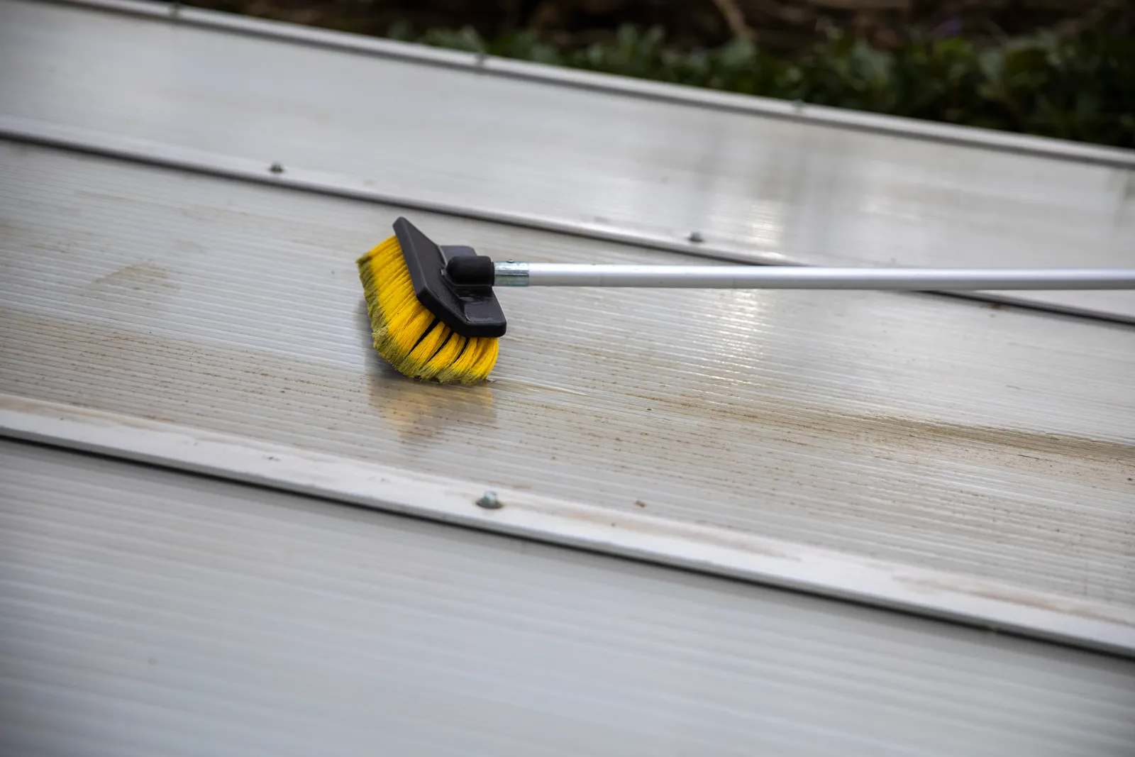 Soft-wash brush on an extension pole cleaning a roof panel