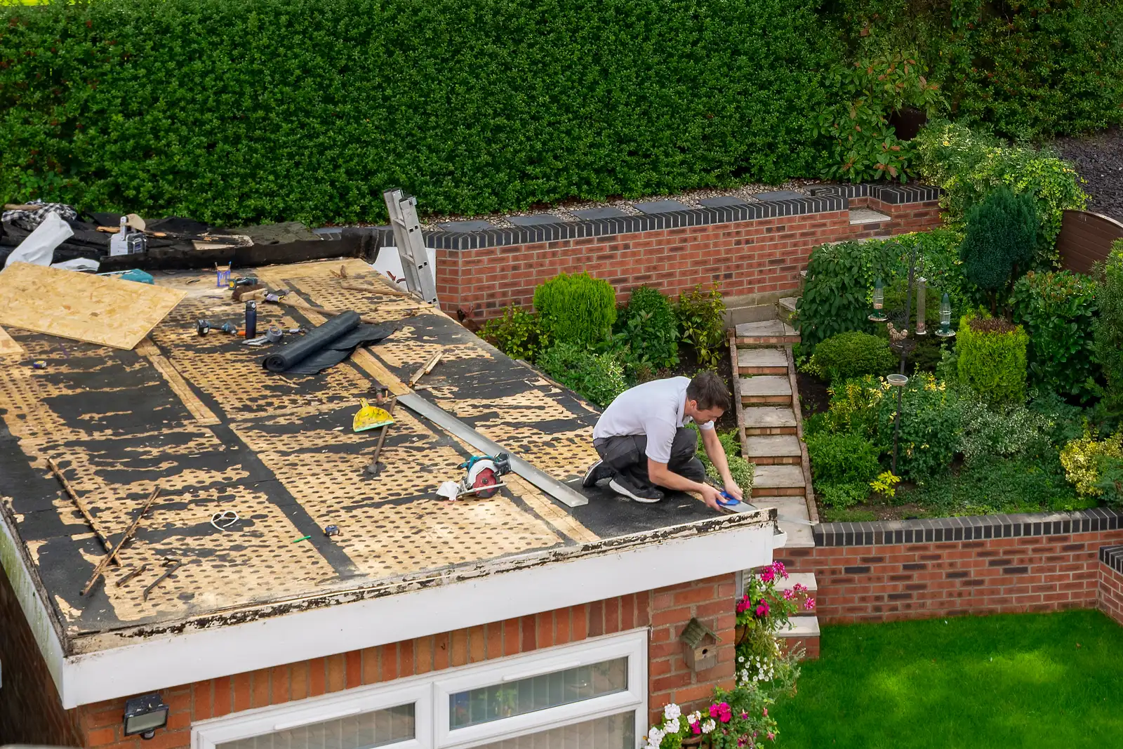 Roofer preparing a garage flat roof with tools and felt membrane laid out in Devizes