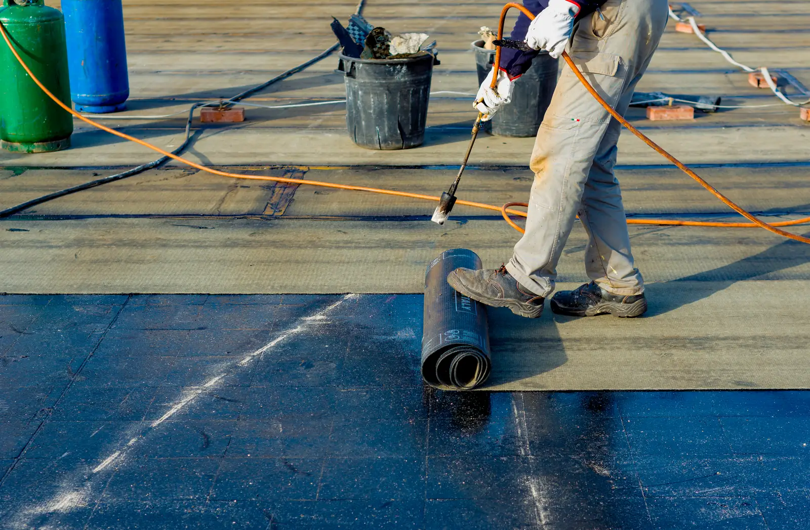Roofer priming a flat roof with a torch ahead of felt membrane installation