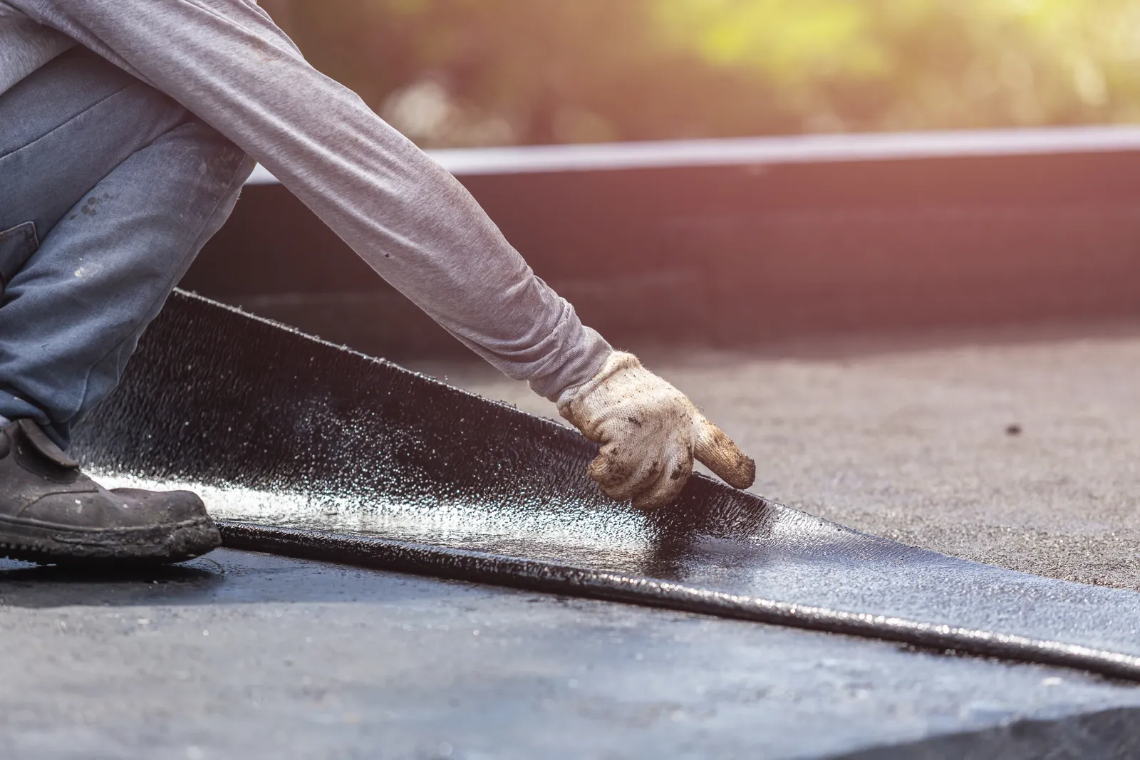Close-up of a roofer smoothing down a freshly torched felt membrane seam