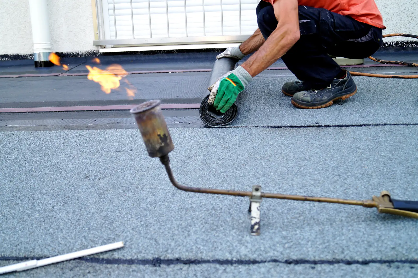Roofer torching a felt membrane seam on a flat roof with a gas blowtorch