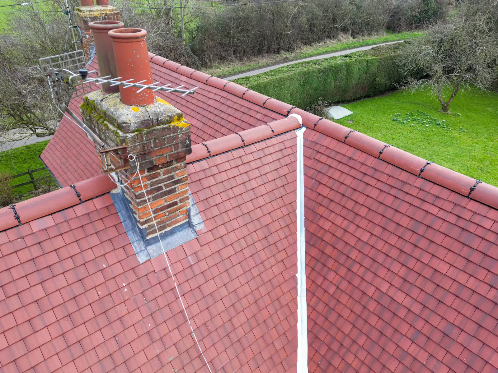 Aerial view of a red clay tile roof with ridge tiles and a brick chimney in Bath