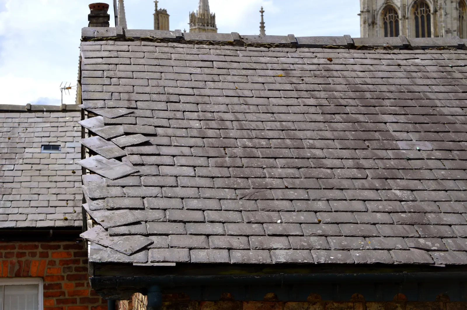 Slipped and displaced roof slates along a ridge, with a cathedral spire behind, in Devizes
